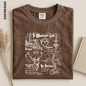 May include: A brown short-sleeved t-shirt featuring a white graphic print with a castle, a heart, a sword, a stag, and a dragon. The text reads: To Whatever End, Terrasen, Fireheart, witch slayer, fire breathing bitch queen, you do not yield, once upon a time, The Thirteen, I will not be afraid, and who loved her kingdom.