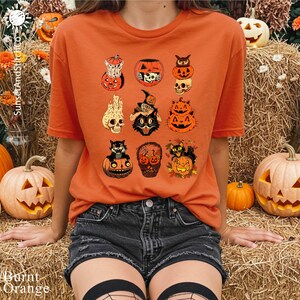 A person wearing an orange t-shirt with a graphic of Halloween pumpkins and bats, sitting on hay bales surrounded by jack-o-lanterns and flowers.