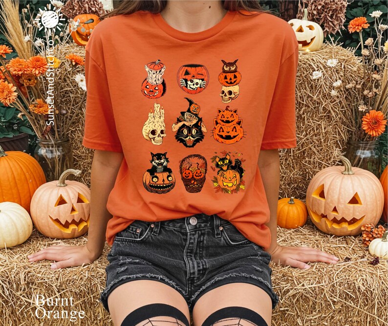 A person wearing an orange t-shirt with a graphic of Halloween pumpkins and bats, sitting on hay bales surrounded by jack-o-lanterns and flowers.