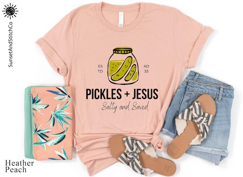 a pink t-shirt with a graphic design, a pair of blue jeans, a pink and green floral bag, and a pair of black and white striped sandals, all laid out on a white background.