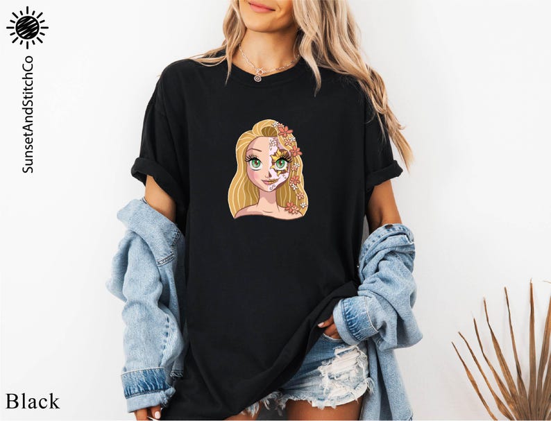 A woman wearing a black t-shirt with a cartoon illustration of a blonde woman with a flower in her hair. She is also wearing a denim jacket and denim shorts.