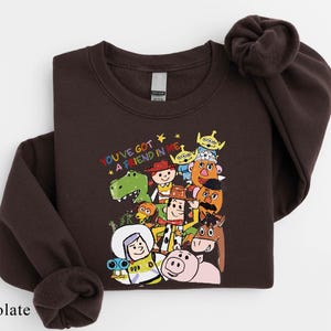 A dark brown sweatshirt with a colorful graphic of various cartoon characters from the Toy Story franchise, including Woody, Buzz Lightyear, and other beloved characters.