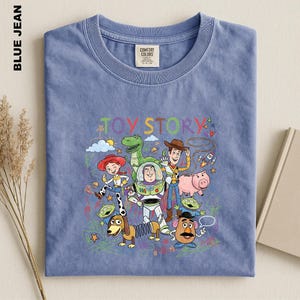 A blue t-shirt with a colorful graphic design featuring characters from the Toy Story movie, including Woody, Buzz Lightyear, and other beloved characters.