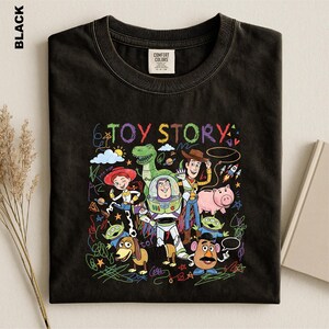 A black t-shirt with a colorful graphic design featuring characters from the Toy Story movie, including Woody, Buzz Lightyear, and other beloved characters.