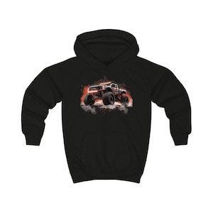 Op de afbeelding: Zwarte hoodie met een afbeelding van een monstertruck in rood, oranje en zwart. De truck wordt in actie getoond, met een wolkeffect eromheen. Het ontwerp is gecentreerd op de voorkant van de hoodie, voor een opvallende look.