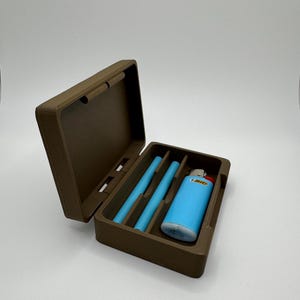 May include: A brown plastic case with a blue lighter and three brown sticks inside. The case has a hinged lid and a small handle.
