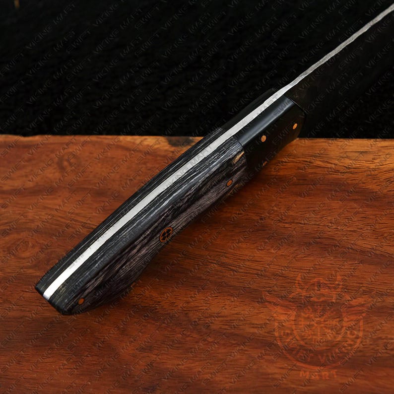 May include: Close-up of a knife with a dark, textured wooden handle and a silver blade. The handle has a black and gray wood grain pattern. The blade is silver with a sharp edge. The knife is on a wooden surface.