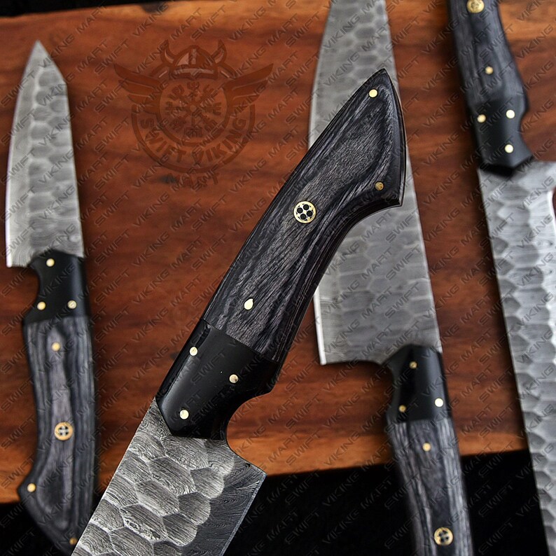 May include: A collection of kitchen knives with textured blades and dark wooden handles. The handles are accented with gold-colored rivets and a decorative emblem. The knives are arranged on a wooden surface, showcasing their craftsmanship.