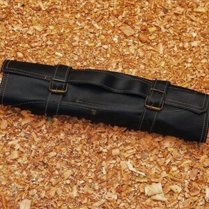 Puede incluir: Rollo de cuchillos de cuero negro con dos correas de hebilla y un asa. El rollo est&aacute; cosido con hilo blanco y est&aacute; sobre virutas de madera. Dise&ntilde;ado para guardar cuchillos, mide unos 30 cm de largo.
