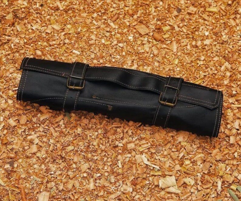 Puede incluir: Rollo de cuchillos de cuero negro con dos correas de hebilla y un asa. El rollo est&aacute; cosido con hilo blanco y est&aacute; sobre virutas de madera. Dise&ntilde;ado para guardar cuchillos, mide unos 30 cm de largo.