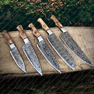 Puede incluir: Seis cuchillos de cocina con mangos de madera y un patrón de hoja de acero Damasco. Los cuchillos están dispuestos en una fila sobre una superficie de madera.