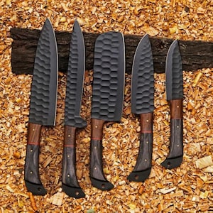 Puede incluir: Un juego de cinco cuchillos de cocina con hojas de color gris oscuro y mangos de madera. Las hojas tienen una superficie texturizada y los mangos combinan madera marr&oacute;n y negra. Los cuchillos est&aacute;n colocados sobre un lecho de virutas de madera.