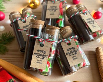 May include: Glass jars with cork stoppers, filled with dark granules and red and green candies. Each jar has a tag that reads "Happy Holidays" and "Love Diana". The jars are tied with red and green twine, and surrounded by Christmas ornaments.