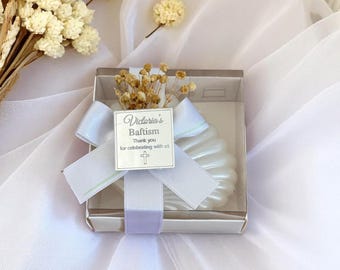 Könnte beinhalten: Ein weißes, muschelförmiges Gastgeschenk in einer transparenten Box, gebunden mit einem hellblauen Band und einem Etikett mit der Aufschrift "Victoria's Baptism". Die Box ist mit Trockenblumen dekoriert.