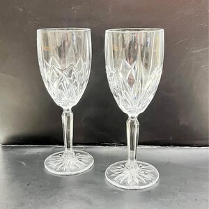 Op de afbeelding: Twee heldere kristallen wijnglazen met een verticaal diamantgeslepen patroon op de kelk, een gefacetteerde zeshoekige steel en een sterpatroon gegraveerd in de ronde voet. De glazen zijn transparant en hebben reflecterende oppervlakken.