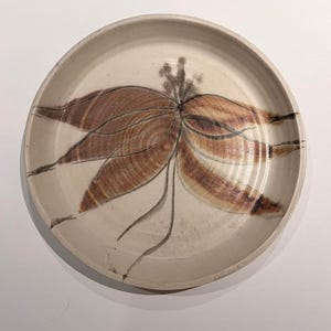 以下が含まれることがあります： オフホワイトの丸い陶器の皿で、茶色とタン色の花の模様が描かれています。 デザインは、濃い茶色の輪郭とアクセントを持つ花びらのような形の中心的なクラスターを特徴としています。 皿にはわずかに盛り上がった縁があります。