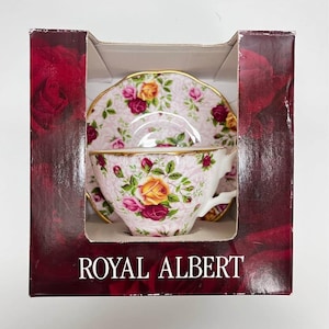 May include: A Royal Albert teacup and saucer set in a box. The set features a pink background with a floral pattern of yellow and red roses. The cup and saucer have gold trim. The box is burgundy with the words "ROYAL ALBERT" in white.