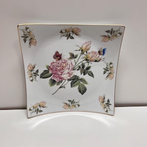 May include: A trio of cream-glazed ceramic mugs with a speckled finish. Each mug is adorned with a hand-painted design: a blue and green leaf, a yellow flower, and a red berry. The mugs have a simple, rounded shape.