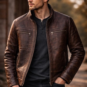 Könnte beinhalten: Braune Lederjacke mit Stehkragen, zwei Brusttaschen mit Reißverschluss und zwei Seitentaschen. Die Jacke wird mit einem dunkelgrauen Hemd und schwarzen Jeans getragen. Ein stilvolles Oberbekleidungsstück.