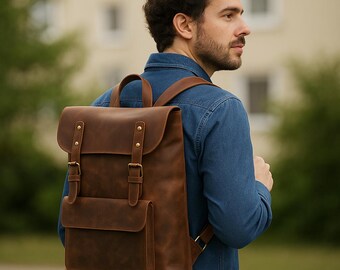 May include: A brown leather backpack with a flap closure, two front pockets, and adjustable straps. The backpack has brass-coloured hardware and a top handle. The bag is worn over the shoulders.
