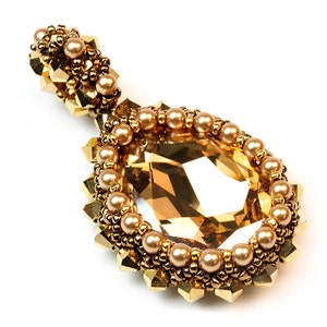 May include: A teardrop-shaped pendant featuring a large, faceted golden-brown crystal center. The crystal is surrounded by a border of small, metallic gold beads and round, lustrous champagne-colored pearls, with additional gold crystal accents.
