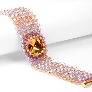 Puede incluir: Un delicado brazalete hecho con cuentas iridiscentes de color rosa y dorado, con una gran piedra preciosa cuadrada facetada de color ámbar en el centro.
