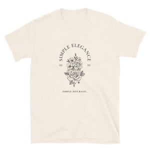 May include: A cream-colored t-shirt with a black graphic design featuring a floral motif and the text "SIMPLE ELEGANCE" in a circle. The text "SIMPLE.NOT.BASIC." is printed below the graphic.