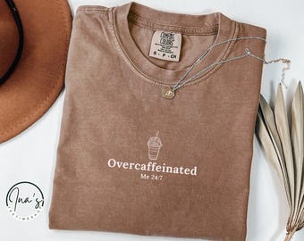 May include: A brown t-shirt with a white graphic of a coffee cup and the text "Overcaffeinated Me 24/7".
