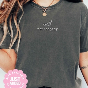 May include: Dark gray t-shirt with the word "neurospicy" and a chili pepper graphic in white. The shirt is a crew neck style and is made of a soft material. The shirt is also available as a sweatshirt.