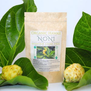 May include: A brown paper bag of "Organic Hawaii Noni Whole Leaf Tea" with green text and a small image of the plant. Two yellow noni fruits and large green leaves surround the bag. The text reads "100% Pure - All Natural - Organic."