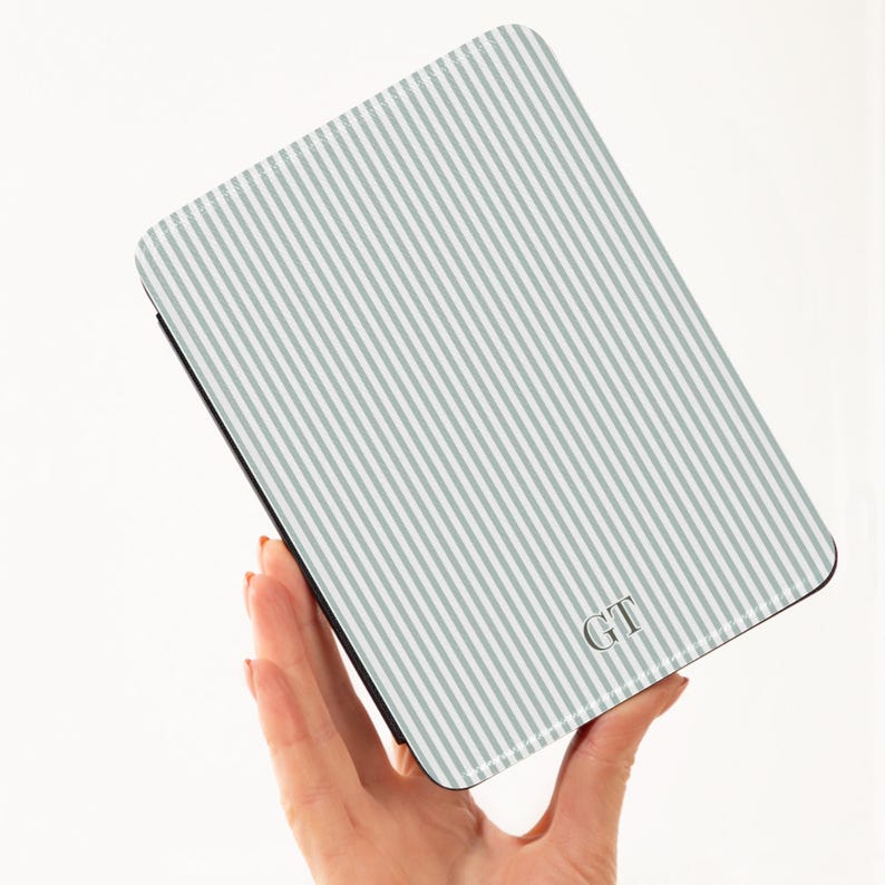 May include: A rectangular case with a light gray and white striped pattern. The case has a black border and the initials "GT" in the lower right corner. The case is held in a person's hand.