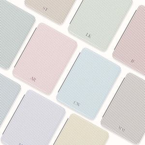 Peut inclure: Plusieurs carnets aux motifs rayés verticaux dans des couleurs pastel, rose, bleu et beige. Chaque carnet, de forme rectangulaire arrondie, présente des initiales dans le coin.