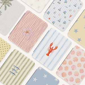 Puede incluir: Una colección de fundas rectangulares para lectores electrónicos con varios patrones, incluyendo una langosta roja sobre rayas azules, una flor de plumeria rosa sobre líneas onduladas, conchas, estrellas azules, peces y motivos náuticos.