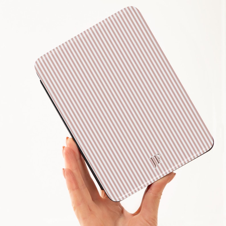 May include: A rectangular case with a striped pattern in shades of pink and white. The case has a black border and a monogram of the letters "JF" in the lower right corner. The case is held by a hand.