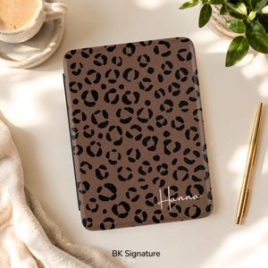 May include: A rectangular e-reader case featuring a brown background with a black leopard print pattern. The name Hanna is printed in white cursive script in the bottom right corner. The case has a textured surface and rounded corners.