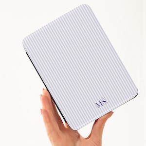 May include: A rectangular case with a white and light purple striped pattern. The case has the initials "MS" in the bottom right corner. The case is held in a person's hand.