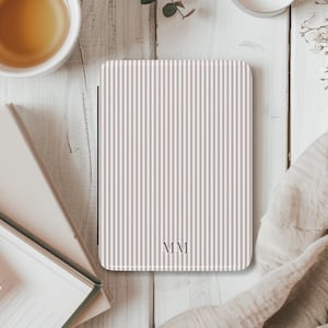May include: A rectangular, striped case in beige and white, with the initials "MM" in the lower right corner. The case is on a white wooden surface, with a cup of tea and a book visible in the background.