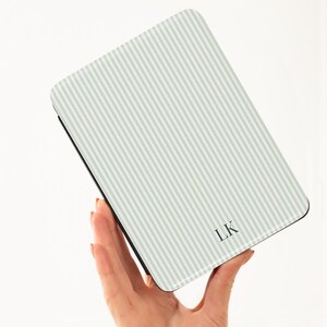 May include: A rectangular case with a light green and white striped pattern. The case has a black border and the initials "LK" in the bottom right corner. The case is held in a person's hand.