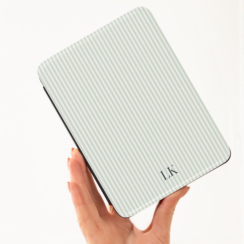May include: A rectangular case with a light green and white striped pattern. The case has a black border and the initials "LK" in the bottom right corner. The case is held in a person's hand.