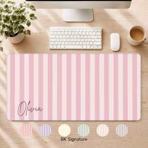 May include: A rectangular desk mat featuring a repeating pattern of vertical light pink and white stripes. The name Olivia is printed in a dark script font on the lower left side of the mat. Below the mat are six circular colour swatches.