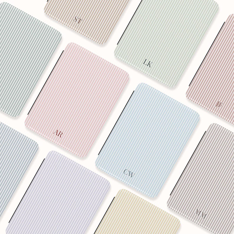 May include: An assortment of rectangular notebooks with vertical striped patterns in various pastel colors, including pink, blue, and beige. Each notebook features a different set of initials in a matching color. The notebooks are arranged on a white background.