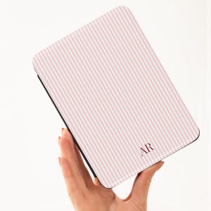 May include: A rectangular case with a pink and white striped pattern. The case has a black border and the initials "AR" in a burgundy color. The case is held in a person's hand.