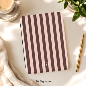May include: A rectangular electronic reader case featuring a vertical striped pattern in alternating shades of dark brown and light pink. The lower center of the case displays the white monogram letters GT. The surface has a textured finish.
