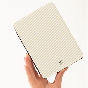 May include: A rectangular case with a cream and beige striped pattern. The case has a black border and the initials "RJ" in the bottom right corner. The case is held in a person's hand.