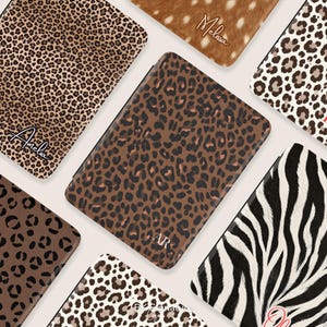 May include: A collection of rectangular e-reader cases featuring various animal print patterns including leopard, cheetah, and zebra designs. Some cases are personalized with names like Amelia and Melissa or initials like AR in script or serif fonts.