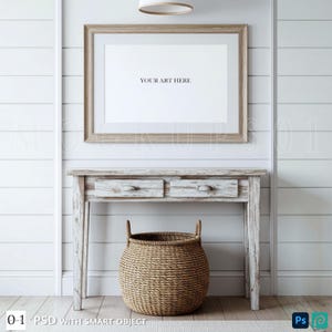 Peut inclure: Une impression encadrée avec le texte "YOUR ART HERE" est suspendue au-dessus d'une console blanche vieillie avec deux tiroirs. Un panier en osier est placé en dessous de la table. Le mur est blanc avec des panneaux horizontaux. Un luminaire est au-dessus du cadre.