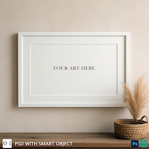 May include: A white rectangular picture frame with the text "YOUR ART HERE" centered on a white background. A woven basket with dried plants sits on a wooden surface. The frame is mounted on a beige wall.