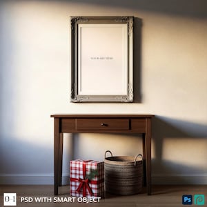 May include: A framed artwork with the text "YOUR ART HERE" above a wooden table. The table has a drawer and is next to a wrapped gift and a woven basket. The frame is silver with ornate detailing.
