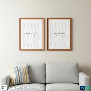 May include: Two framed art prints with a copper-colored frame, each displaying a white background with a pattern of diagonal lines and the text "YOUR ART HERE". Below, a gray sofa with a striped pillow.