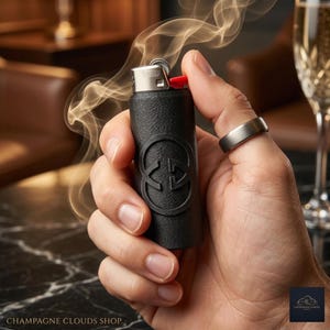 May include: A black lighter with a red ignition button, encased in a textured black sleeve with a circular logo. Smoke rises from the lighter. The text "CHAMPAGNE CLOUDS SHOP" is at the bottom.